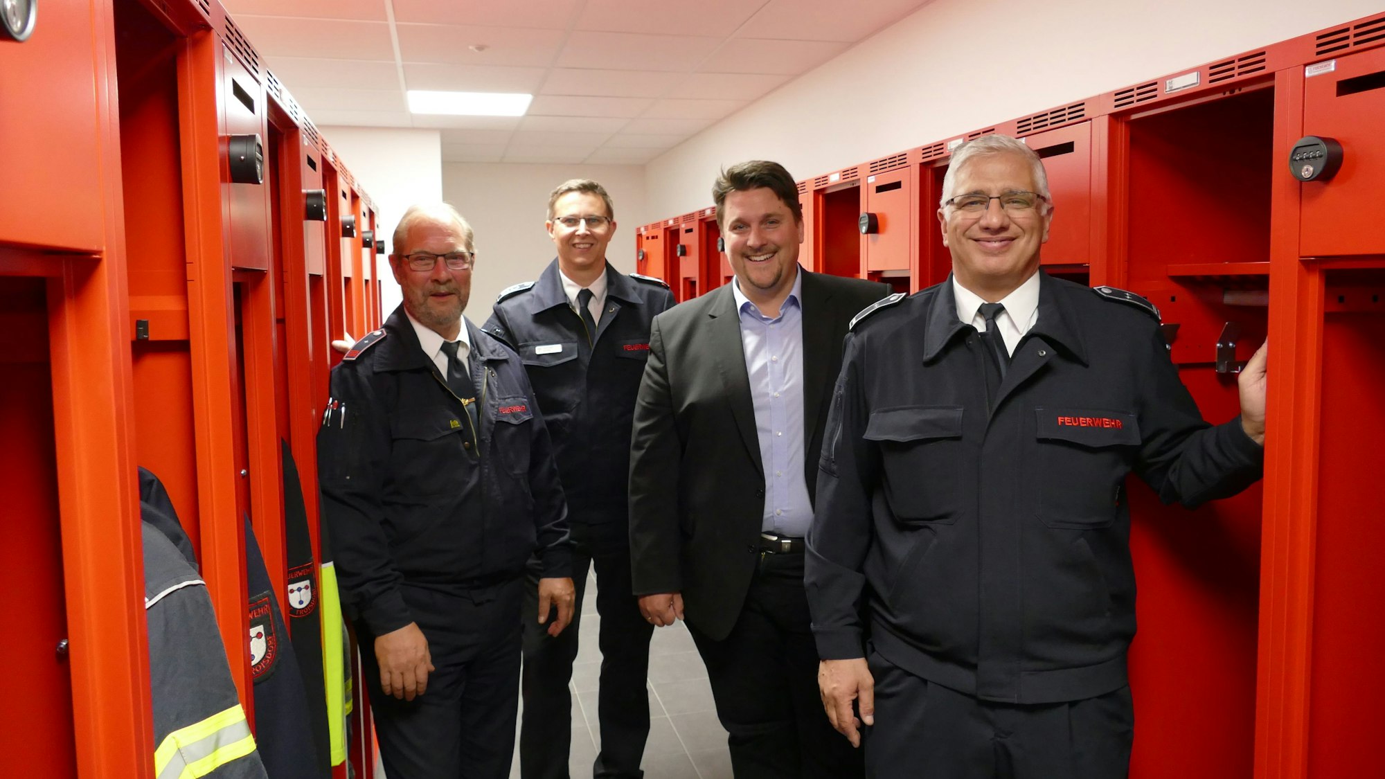Zu sehen sind Löschgruppenführer Ralf Eich, Leiter der Troisdorfer Feuerwehr, Lars Gödel, Bürgermeister Alexander Biber und Löschgruppenführer Salvatore Rizzello zwischen roten Schränken.