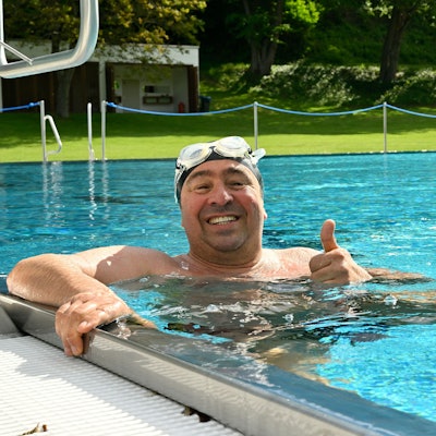 Ein Mann hält sich am Beckenrand des Schwimmeckens fest.