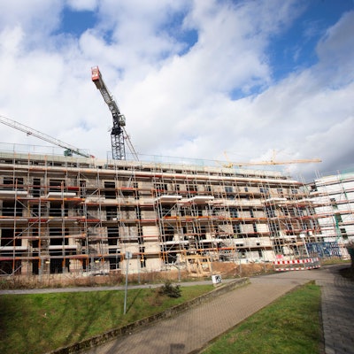 Ein Gebäudekomplex, der im Bau inbegriffen ist, ist mit einem Gerüst umstellt - im Hintergrund ragen Baukräne auf. (Symbolbild).
