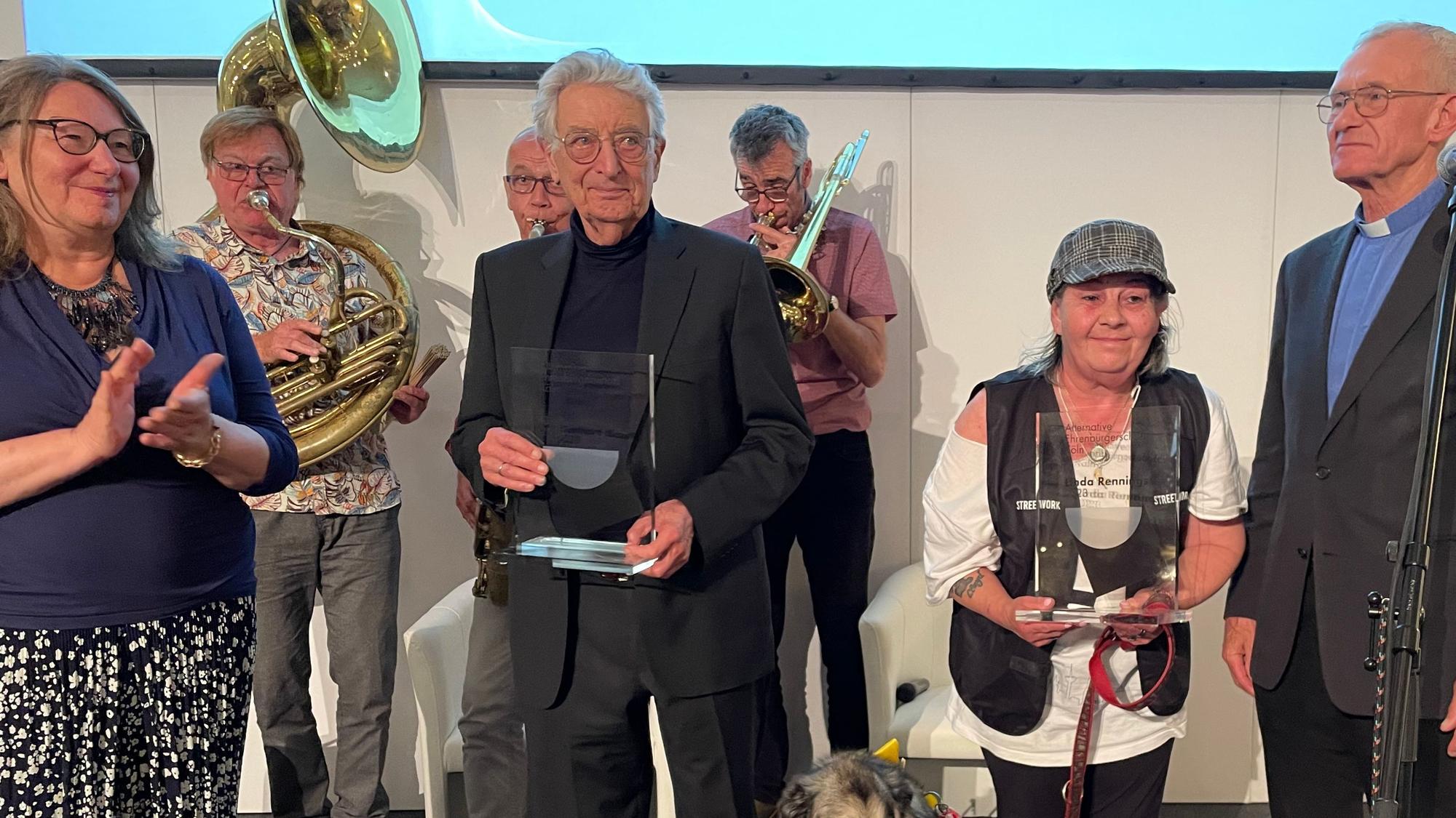 Für ihren Kampf um Menschenrechte geehrt wurden Gerhart Baum und Linda Rennings (2. und 3. v. links). Überreicht wurden die Preise von Irene Franken, Mitgründerin des Frauengeschichtsvereins (l.) und Pfarrer Franz Meurer. Beide wurden in den Vorjahren mit der "Alternativen Kölner Ehrenbürgerschaft" ausgezeichnet. Alle vier stehen nebeneinander auf dem Podium und freuen sich.