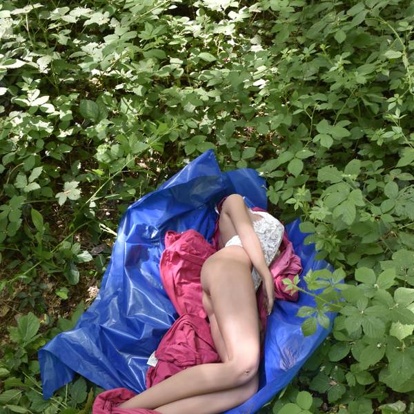 Eine lebensgroße Puppe liegt auf einem Müllsack in einem Gebüsch.