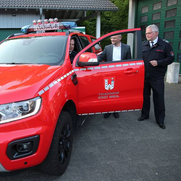 Drei Männer stehen an einem knallroten Feuerwehrauto in Form eines SUV.