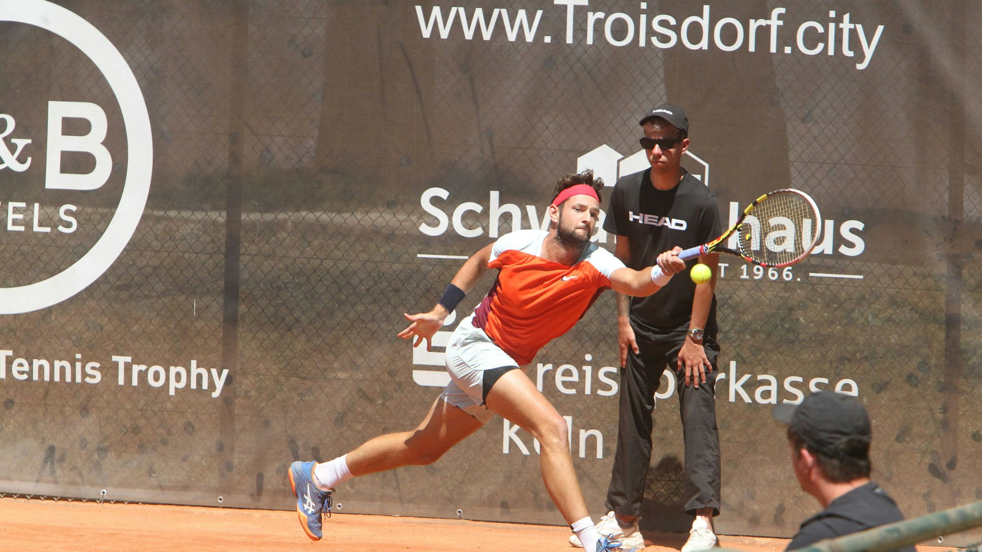 Ein Mann spielt Tennis auf einem Sandplatz.