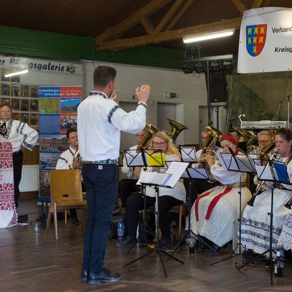 Ein Dirigent leitet ein Blasorchester, das in siebenbürgischer Tracht gekleidet ist.