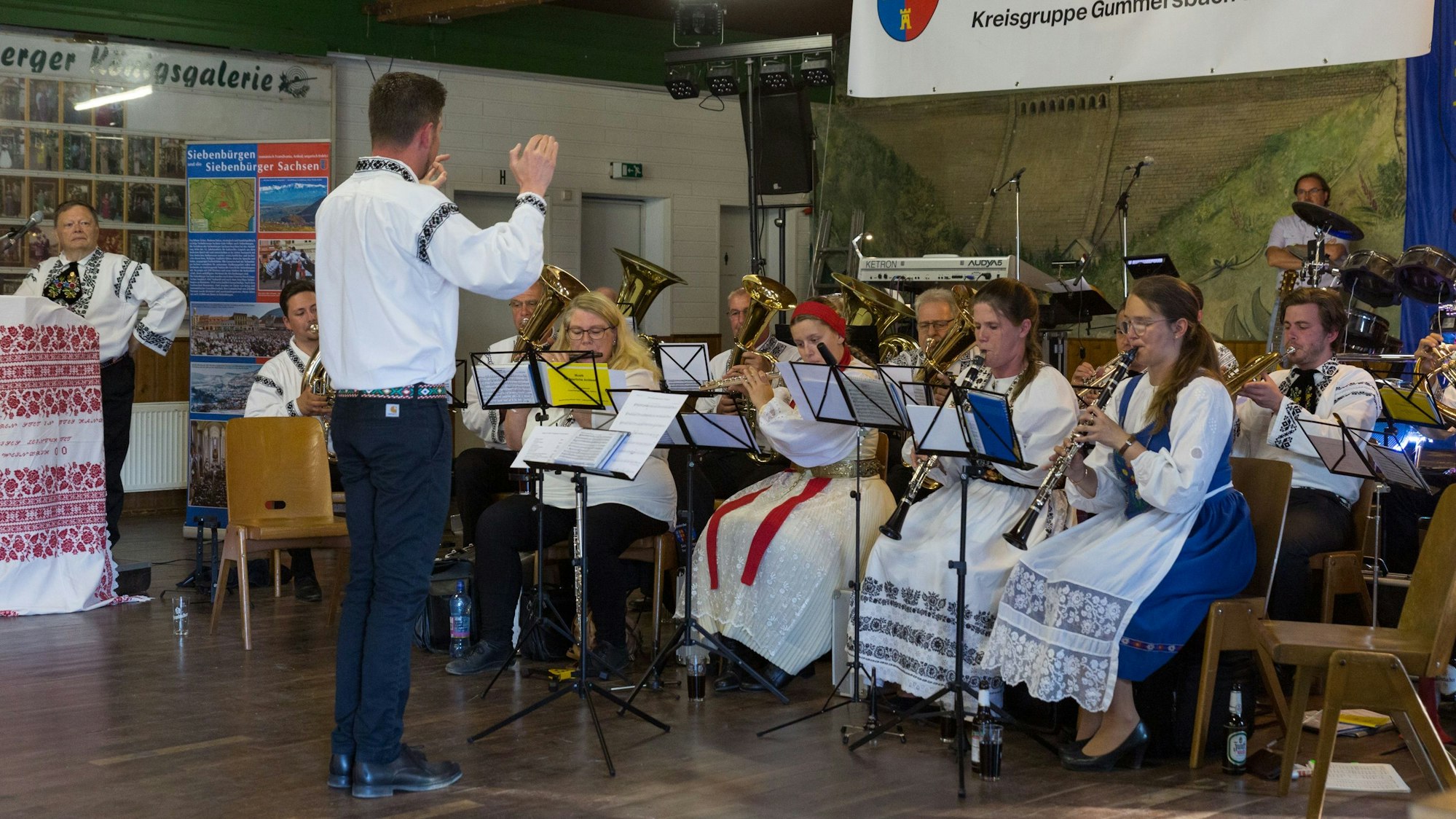Ein Dirigent leitet ein Blasorchester, das in siebenbürgischer Tracht gekleidet ist.