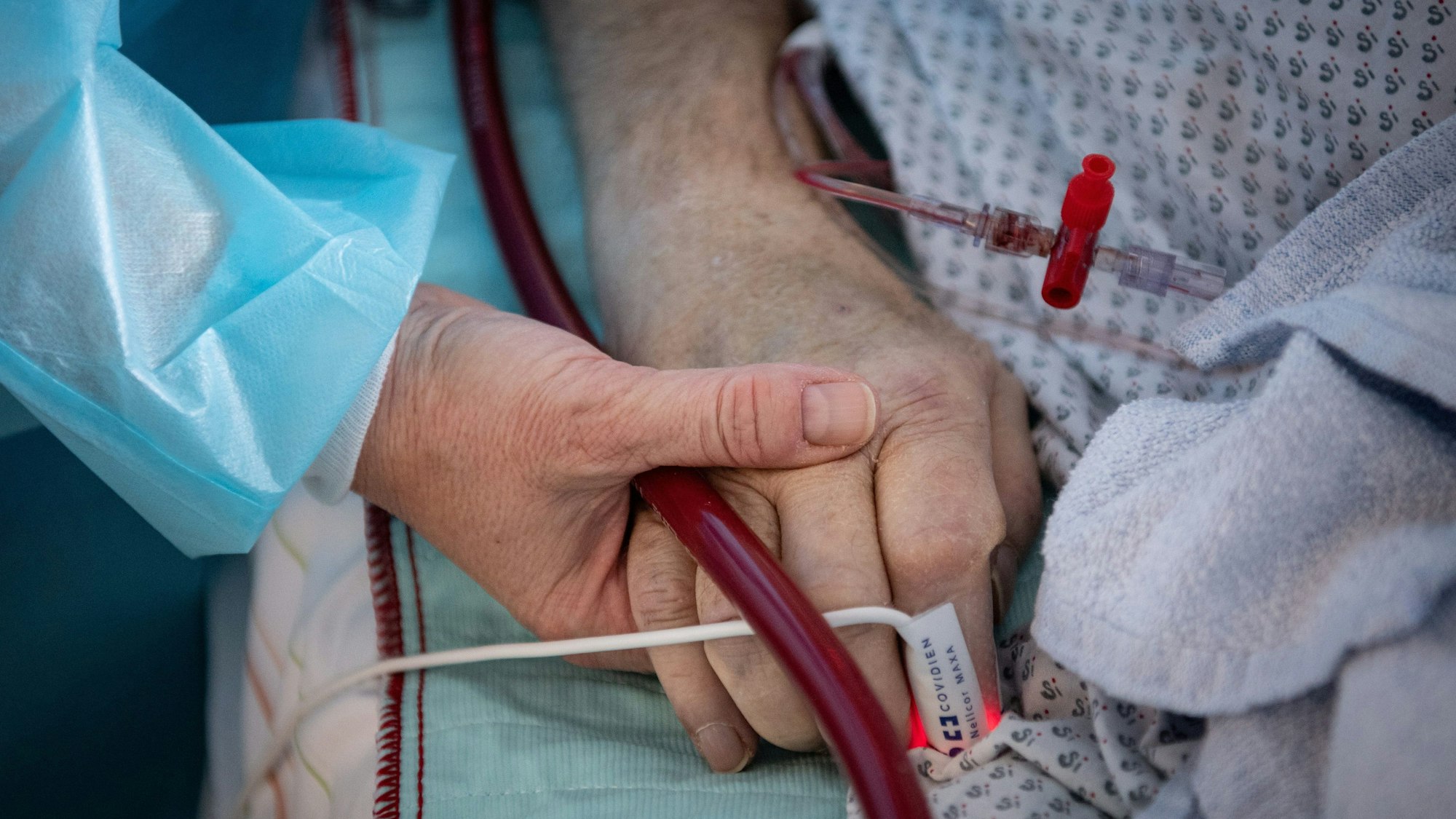 Eine Krankenschwester versorgt einen schwer an Corona erkrankten Patienten einer Intensivstation und hält dabei die Hand des Mannes.