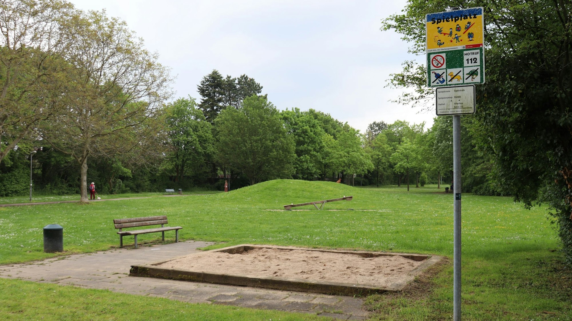 Der Spielplatz Jasminweg mit einem Sandkasten, einer Wippe und grüner Wiese.