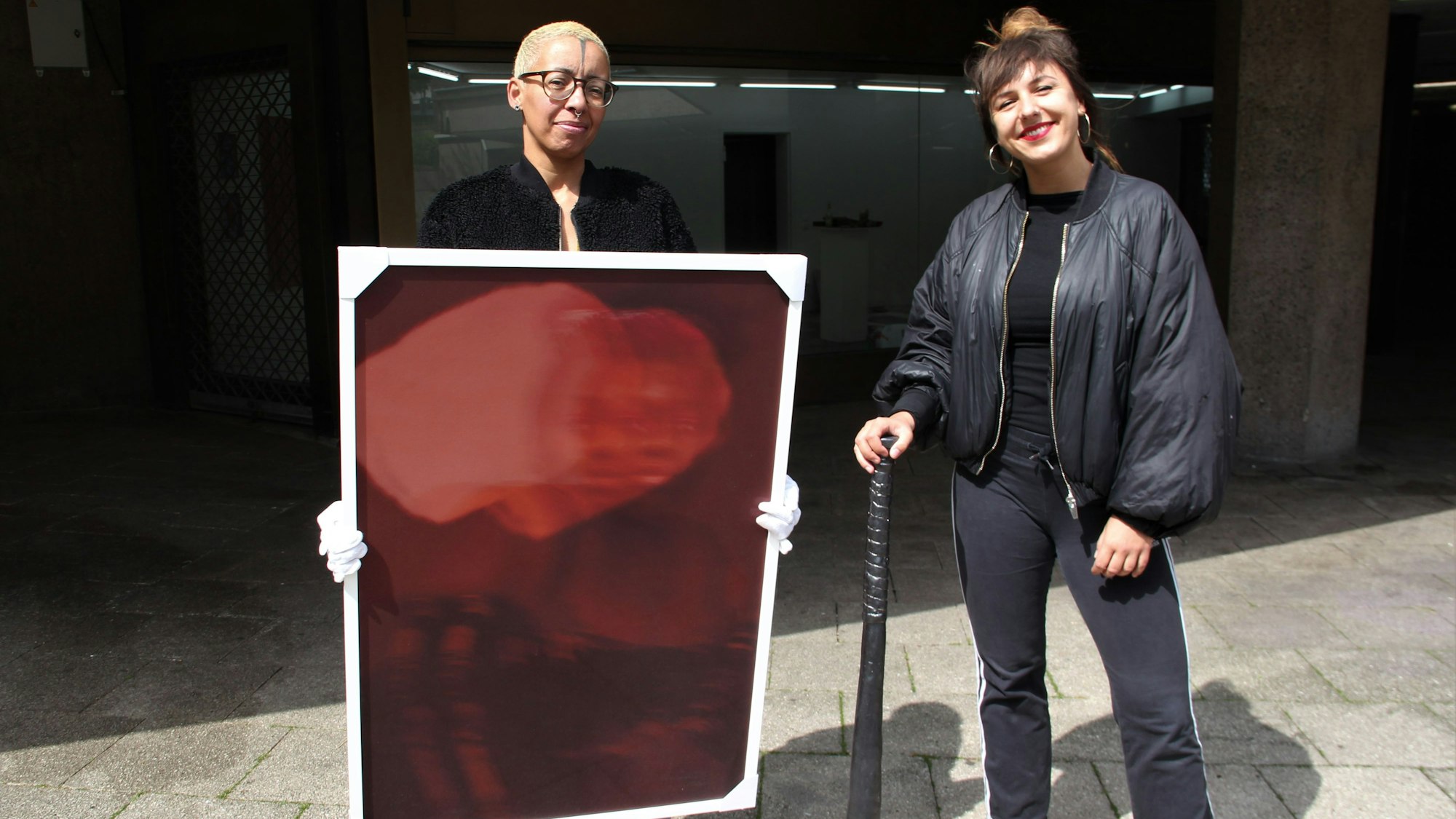 Die Künstlerinnen Nora Hase (l.) und Marleen Rothaus zeigen ihre Werke, ein Gemälde und ein Keramik-Baseballschläger.