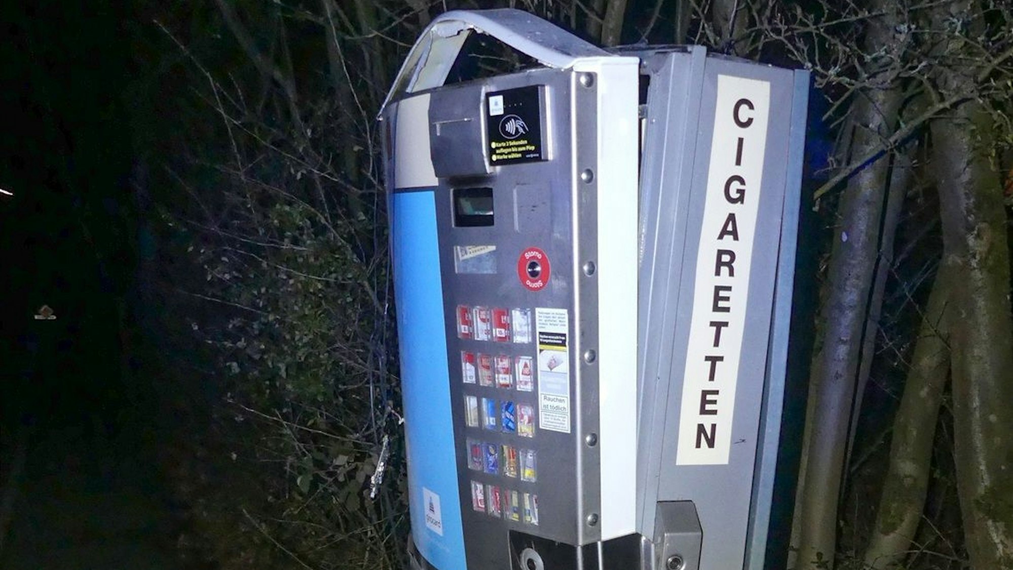 Ein aufgesprengter Zigarettenautomat wird mit Blitzlicht im Dunkeln angeleuchtet.
