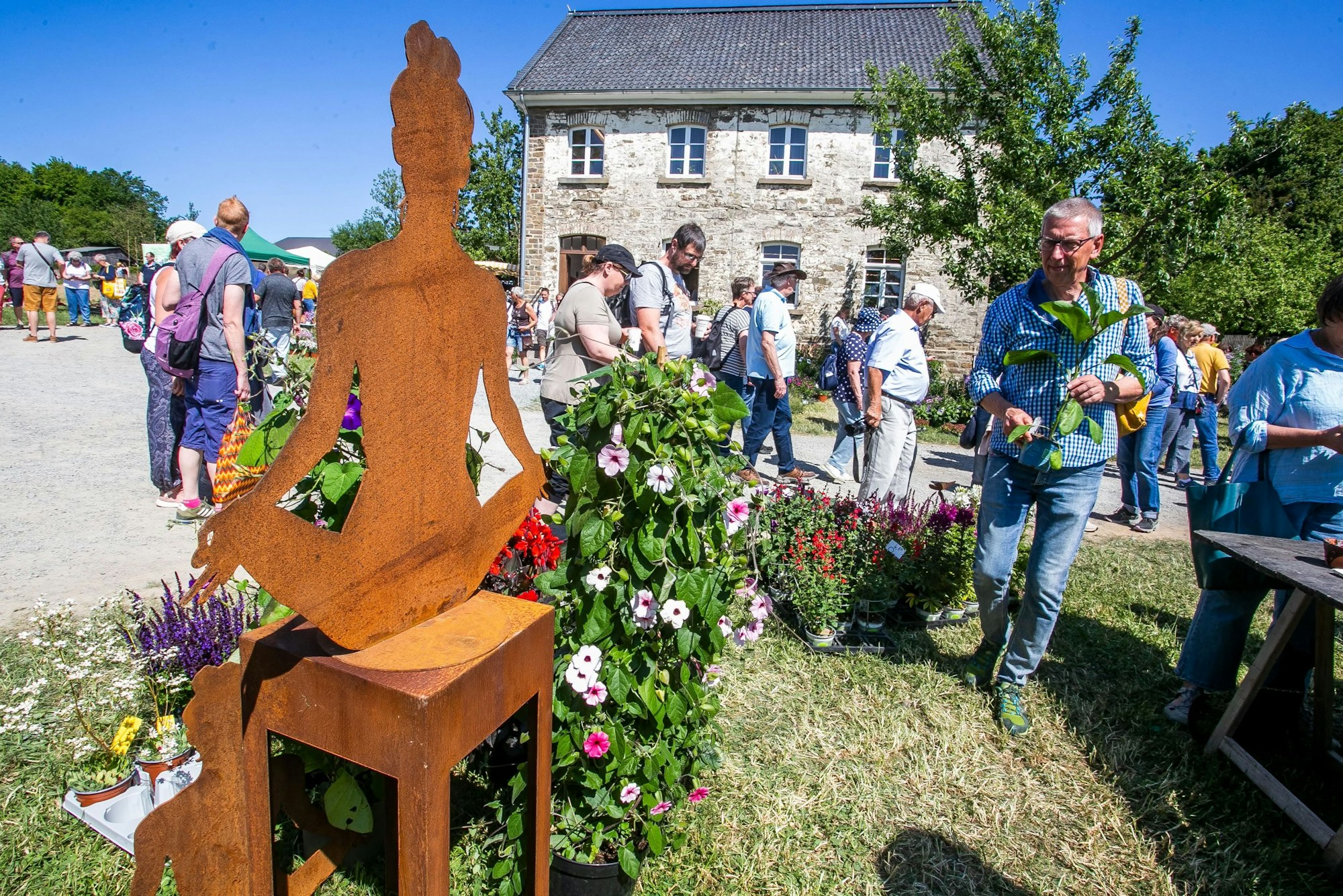 Mehrere Menschen sind auf dem Gelände des Lindlarer Freilichtmuseums unterwegs - im Vordergrund steht Gartendekoration.