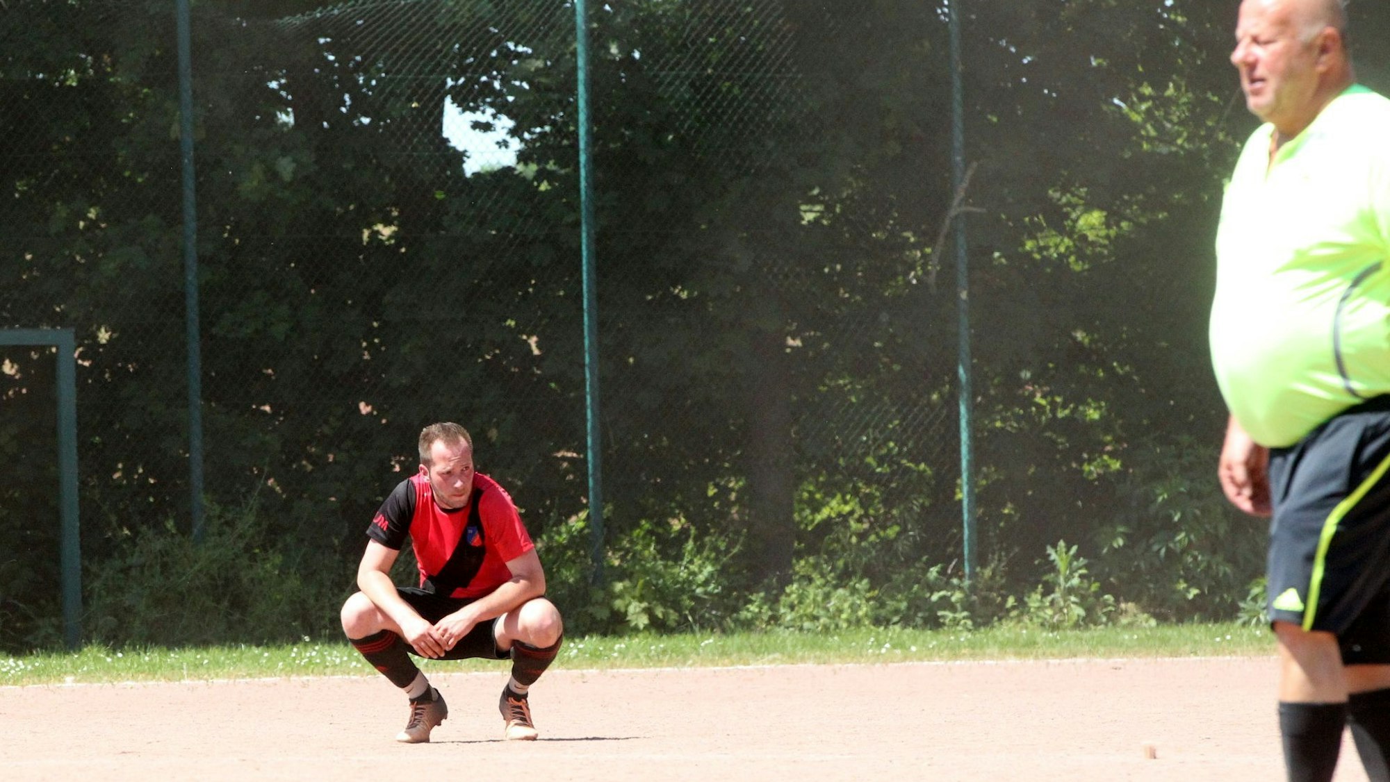 Weyers Spieler Jan Lodzinski hockt fassungslos auf dem Aschenplatz in Scheven. Von rechts kommt der Schiedsrichter ins Bild.