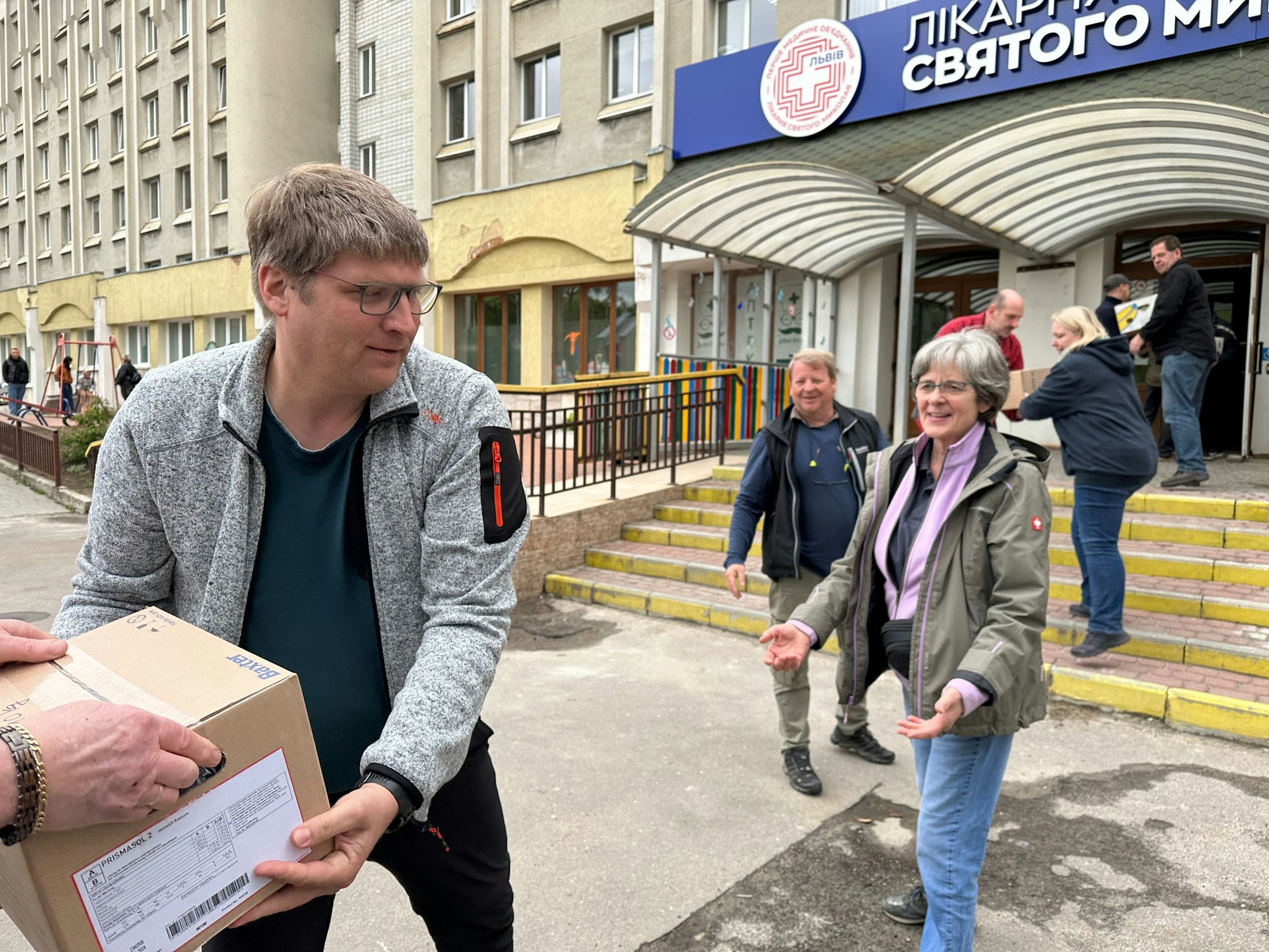 Männer und Frauen reichen Parkete vor einem Krankenhauseingang in einer Menschenkette weiter.
