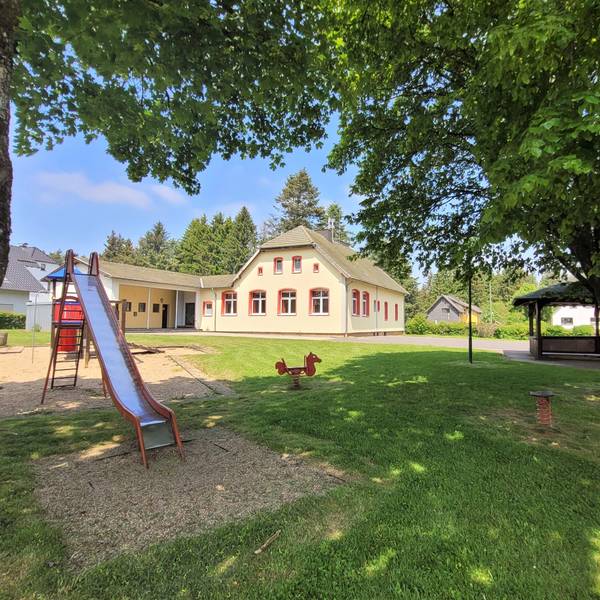 Das Bild zeigt den Dorfplatz in Broich mit einer Rutsche und einem Grillplatz. Im Hintergrund ist das Dorfgemeinschaftshaus zu sehen.