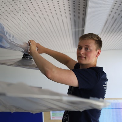 Der Student Bastian Scho greift mit beiden Händen an ein Rohr, das zu einer Lüftungsanlage gehört.