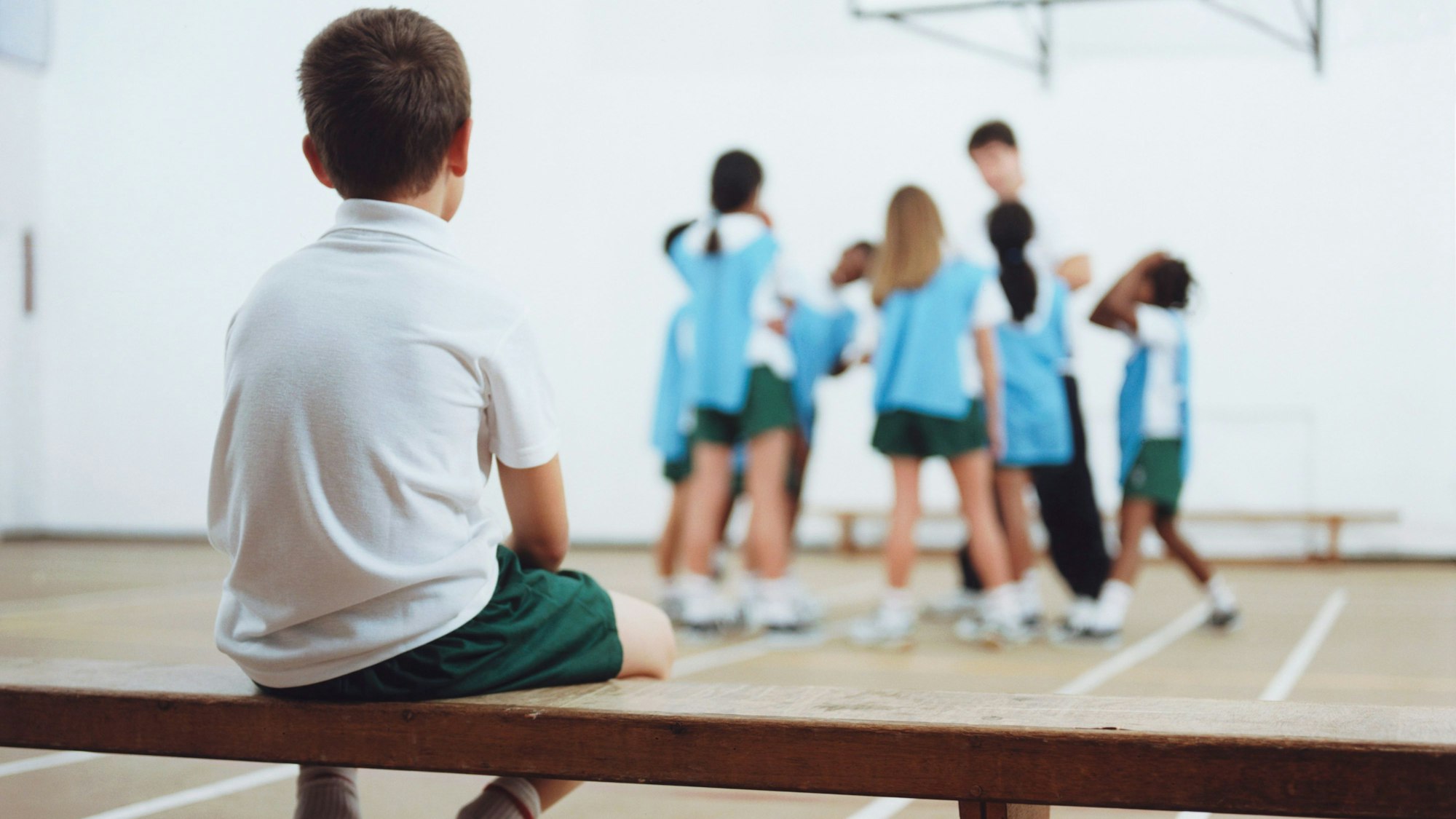 Ein kleiner junge sitzt alleine auf der Bank im Sportunterricht.