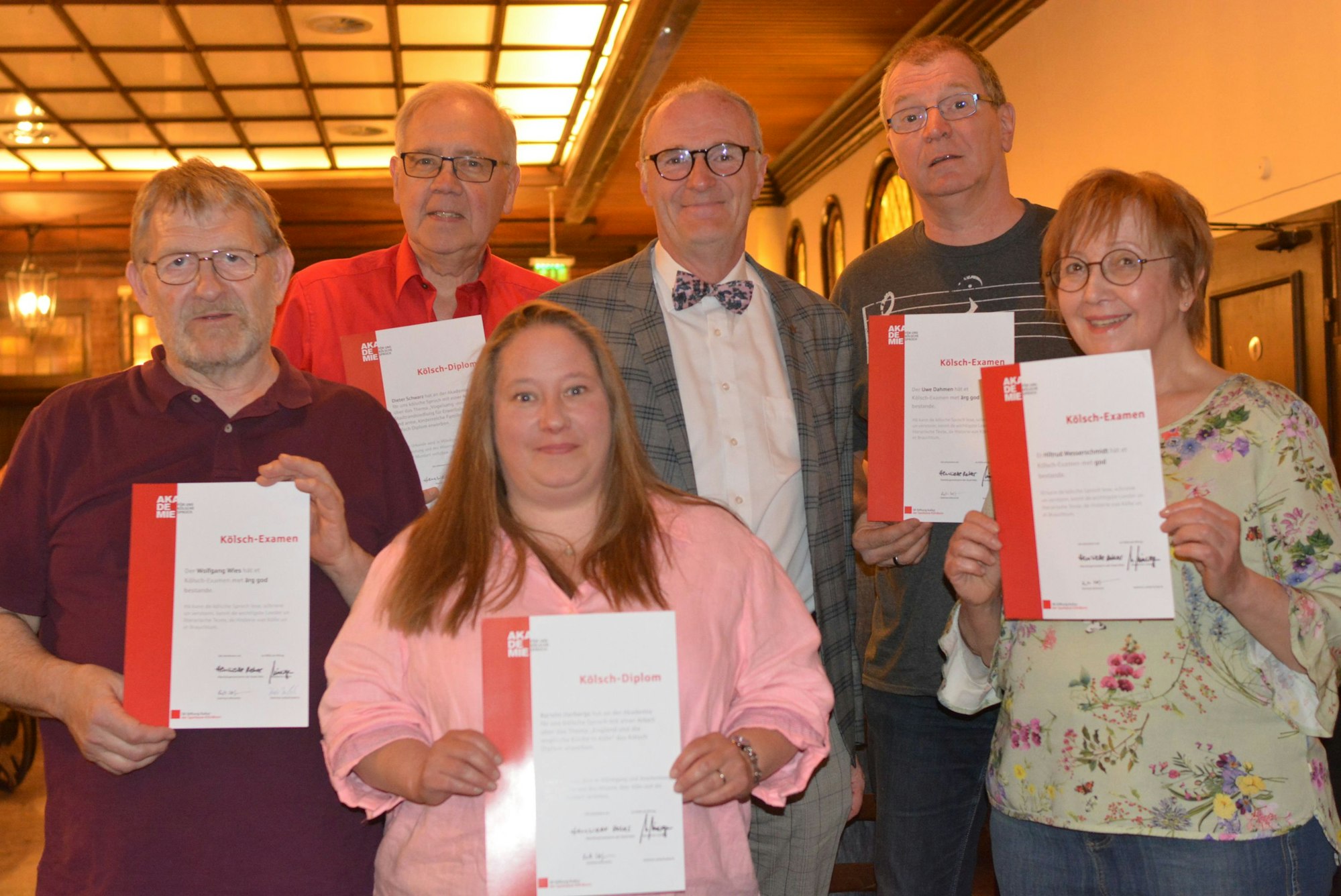 Sechs Personen stehen für ein Gruppenfoto zusammen. Fünf halten ihr Examen in die Kamera.