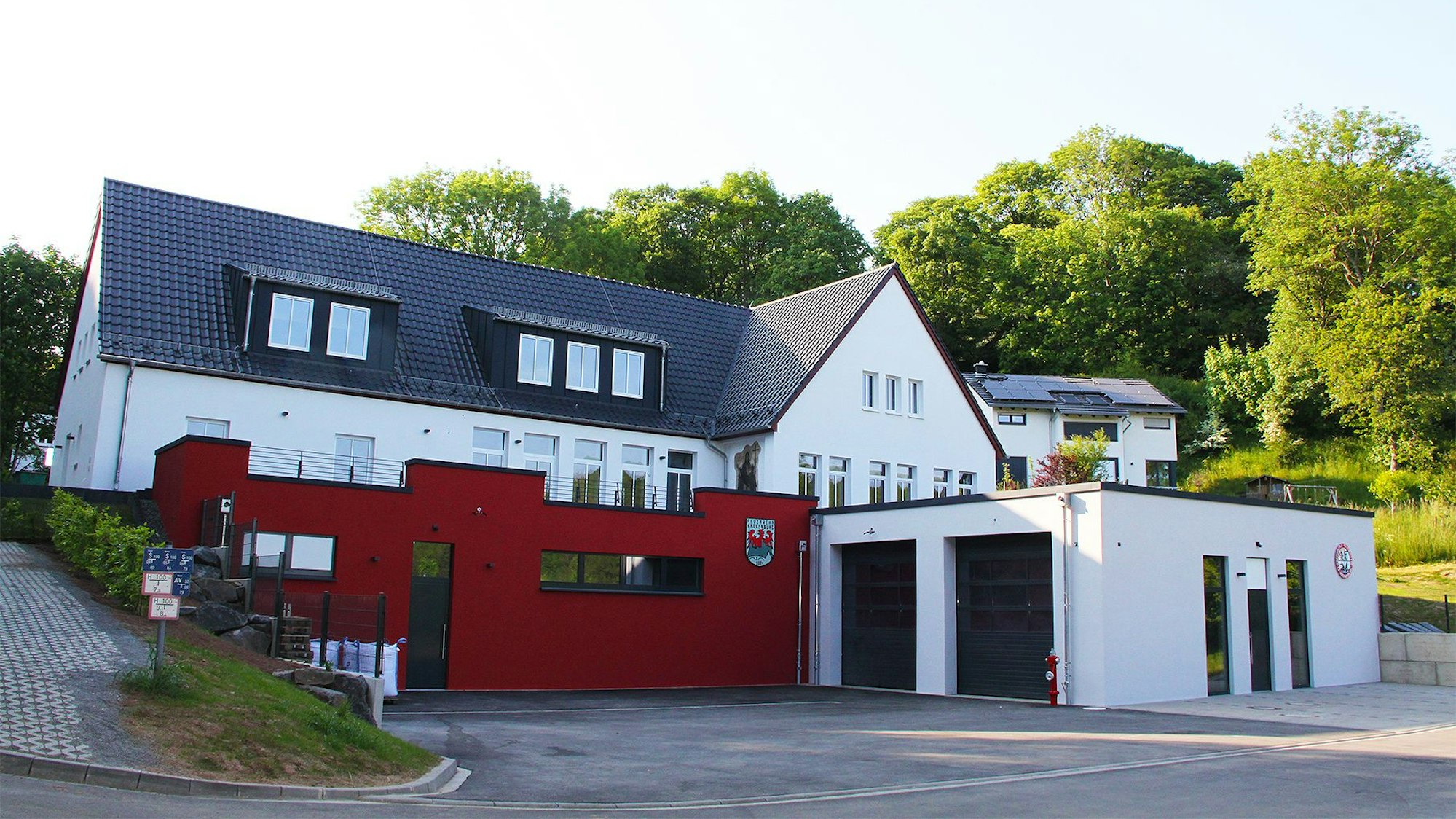 Das Bild zeigt vorne den Neubau des Feuerwehrgerätehauses in Kronenburg, dahinter und etwas erhöht im Hang das Dorfgemeinschaftshaus.