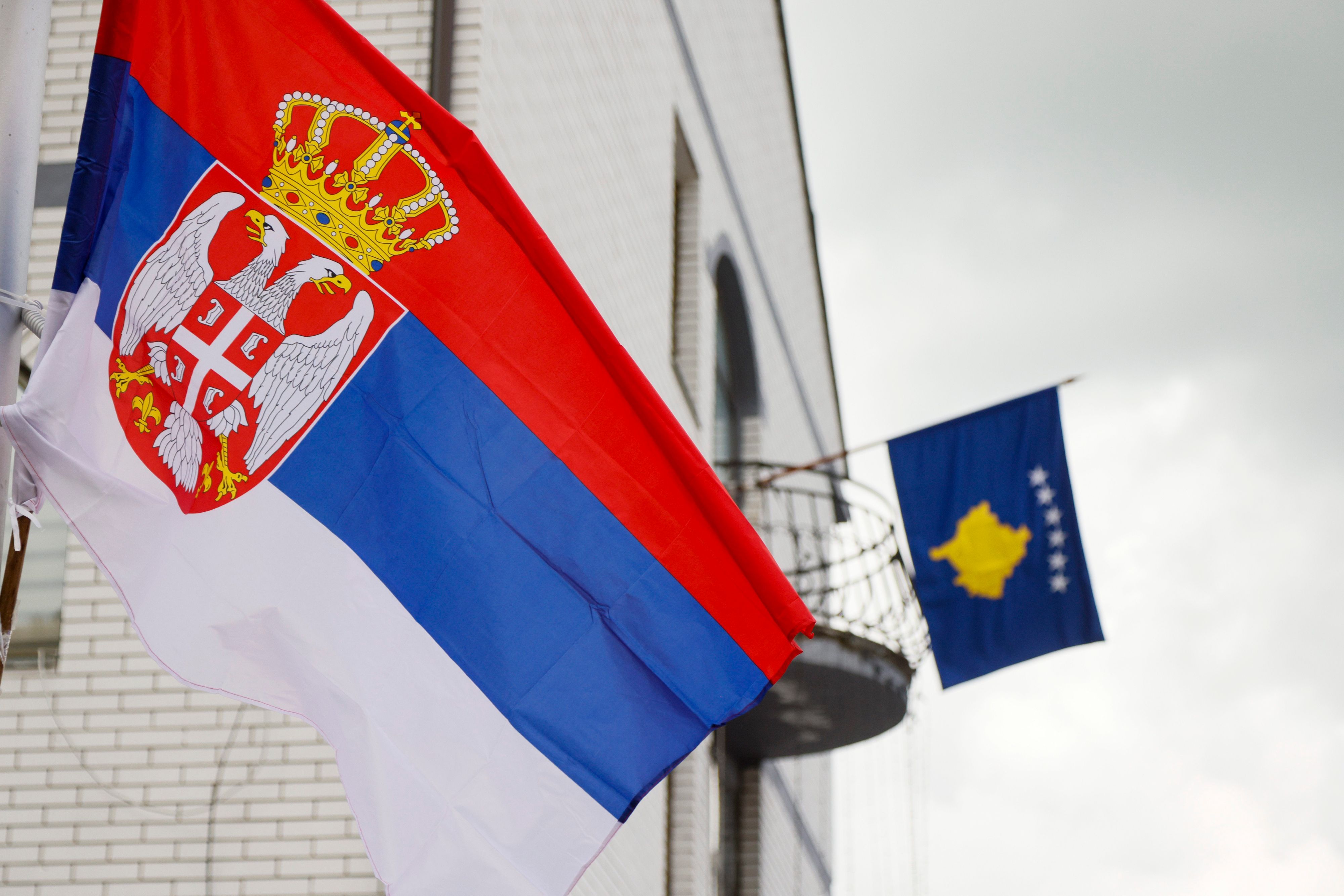 Die serbische Flagge weht an einem Laternenpfahl vor einer Flagge des Kosovo am Rathaus.