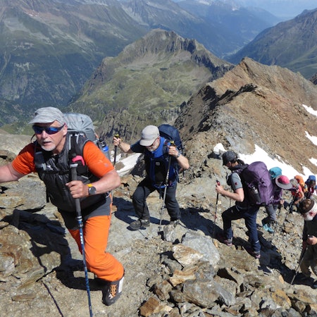 Mehrere Wanderer besteigen, mit Rucksäcken auf dem Rücken und Stöcken in der Hand, einen steinigen Berg.