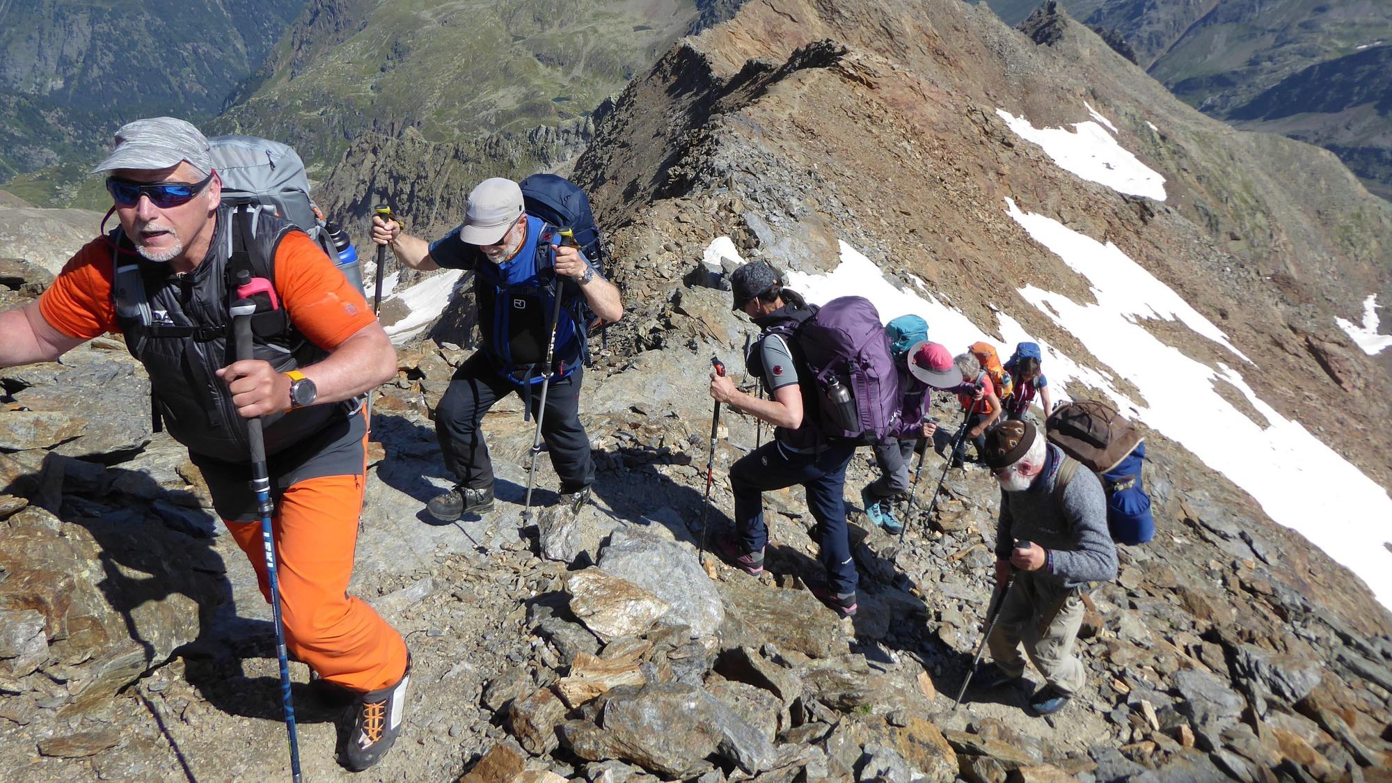 Mehrere Wanderer besteigen, mit Rucksäcken auf dem Rücken und Stöcken in der Hand, einen steinigen Berg.