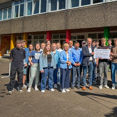 Zu sehen ist eine Menschengruppe, in deren Mitte drei Männer einen großen Scheck halten.