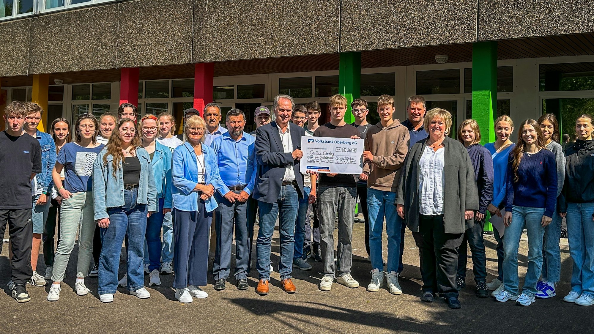 Zu sehen ist eine Menschengruppe, in deren Mitte drei Männer einen großen Scheck halten.