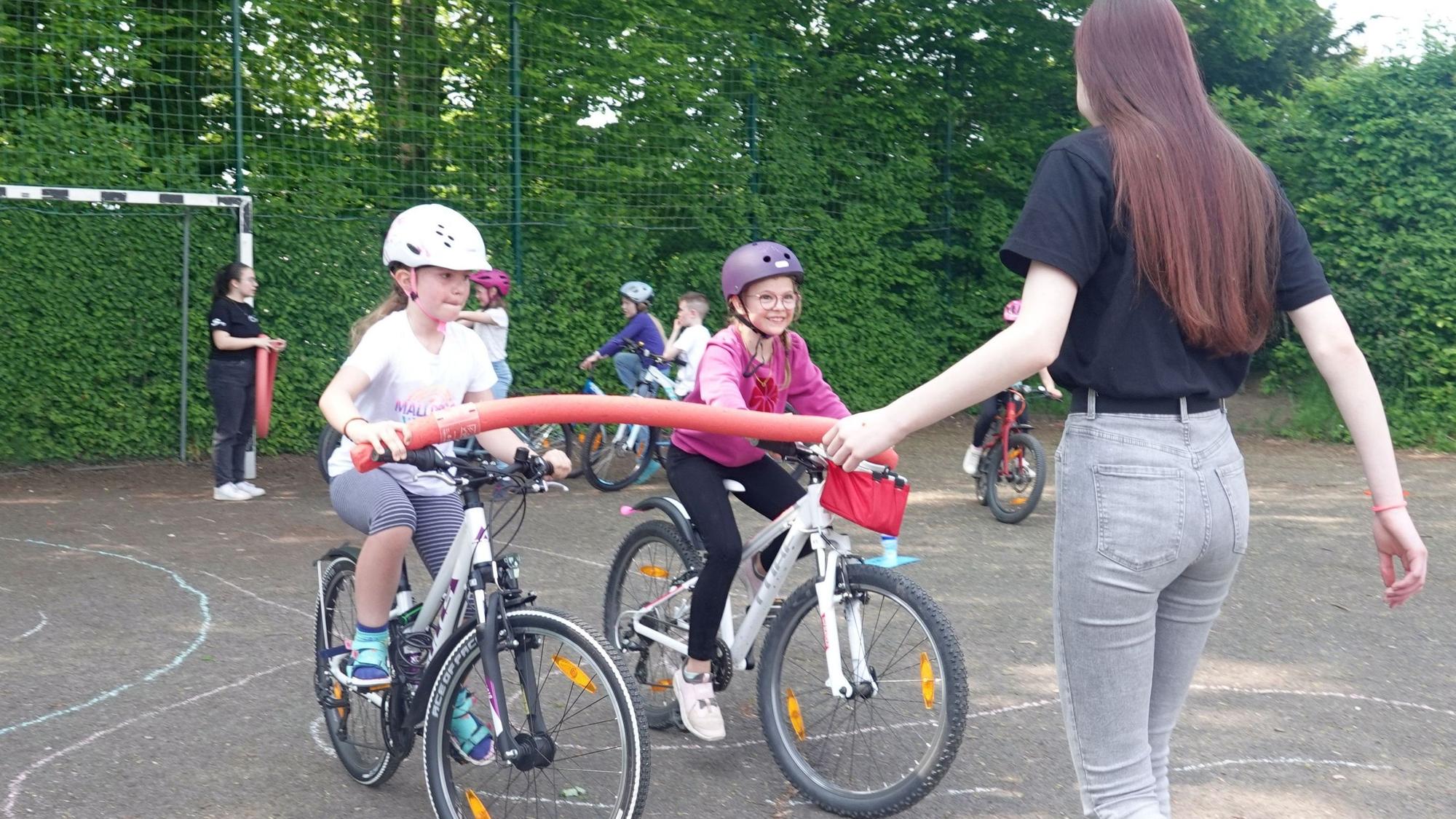 Zwei Mädchen üben unter Anleitung einer jungen Frau das Fahrradfahren.