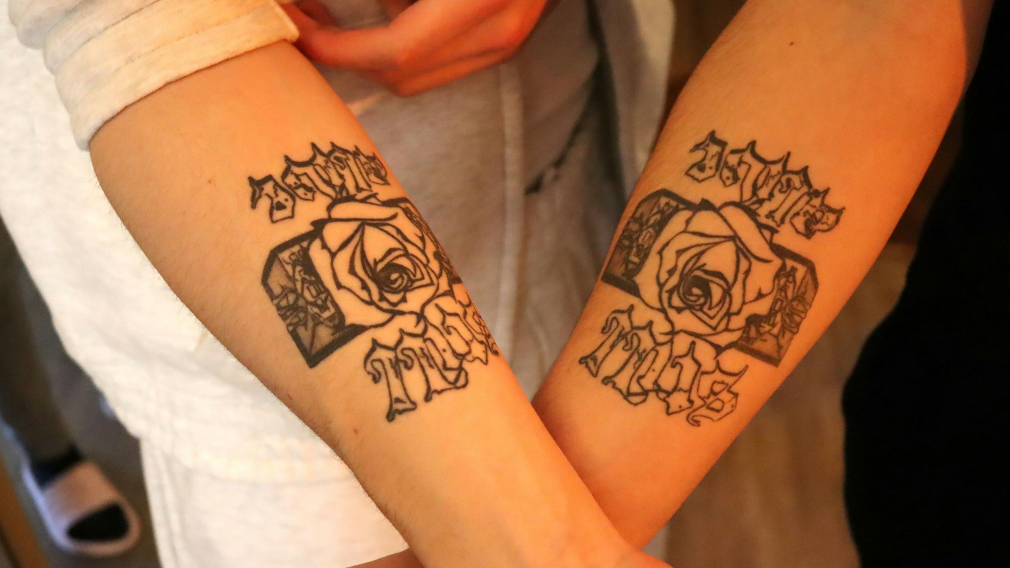 Liaze und MTJ zeigen ihre Arme, auf die sie den Namen des Labels Still Alive und das Logo, eine Rose, die aus Betonbauten wächst, tätowiert haben.