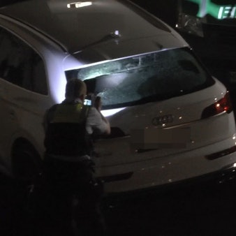 Ein weißes Fahrzeug wird von Polizisten untersucht.