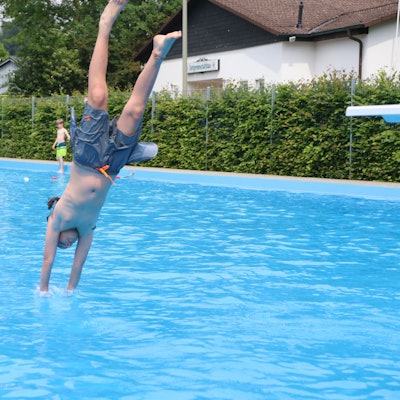 Ein Junge macht in einem Freibad einen Köpper ins Wasser.
