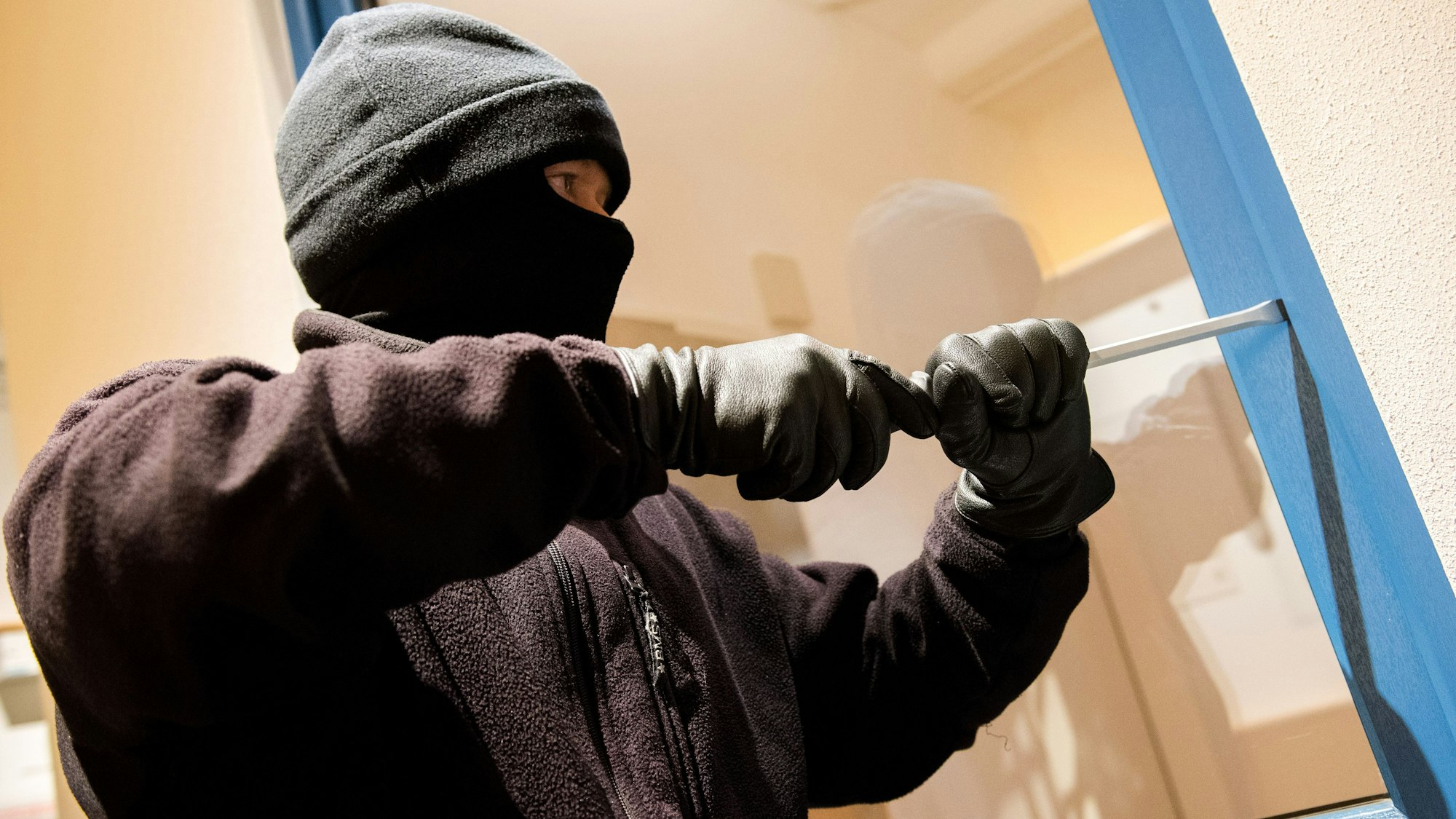 Ein als Einbrecher verkleideter Mann hebelt in der Kriminalpolizeilichen Beratungsstelle der Polizei ein Fenster auf.