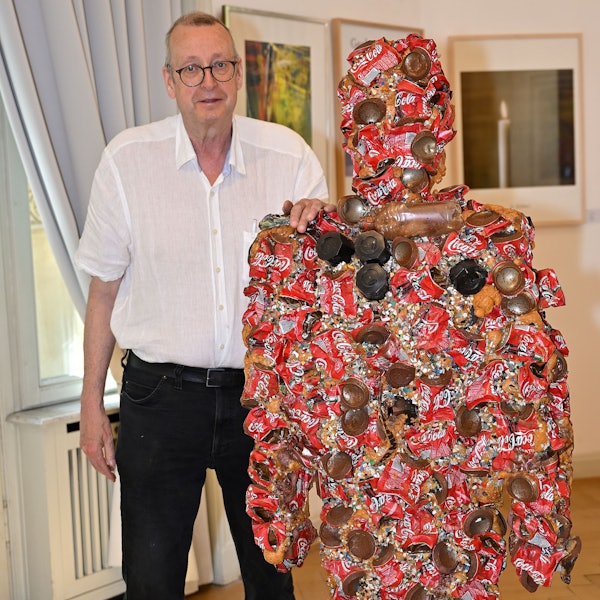 Dirk Kästel steht neben einem Kunstwerk, das HA Schult für die Ausstellung gespendet hat.