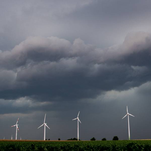 Eine Unwetterfront und dunkle Wolken ziehen über den Himmel. Davor ragen fünf Windräder in den Himmel.