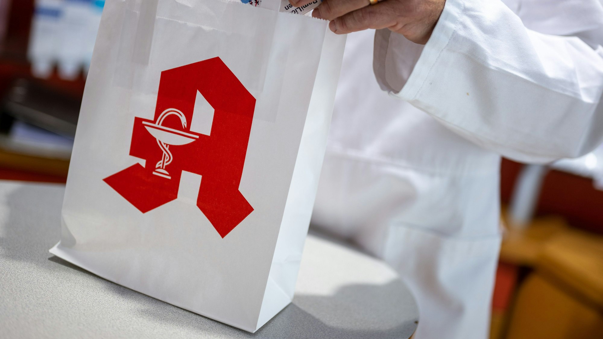 ILLUSTRATION - 05.06.2023, Berlin: Ein Apotheker legt in einer Apotheke eine Packung mit Tabletten in eine Papiertasche mit Apotheken-Logo. Foto: Monika Skolimowska/dpa +++ dpa-Bildfunk +++