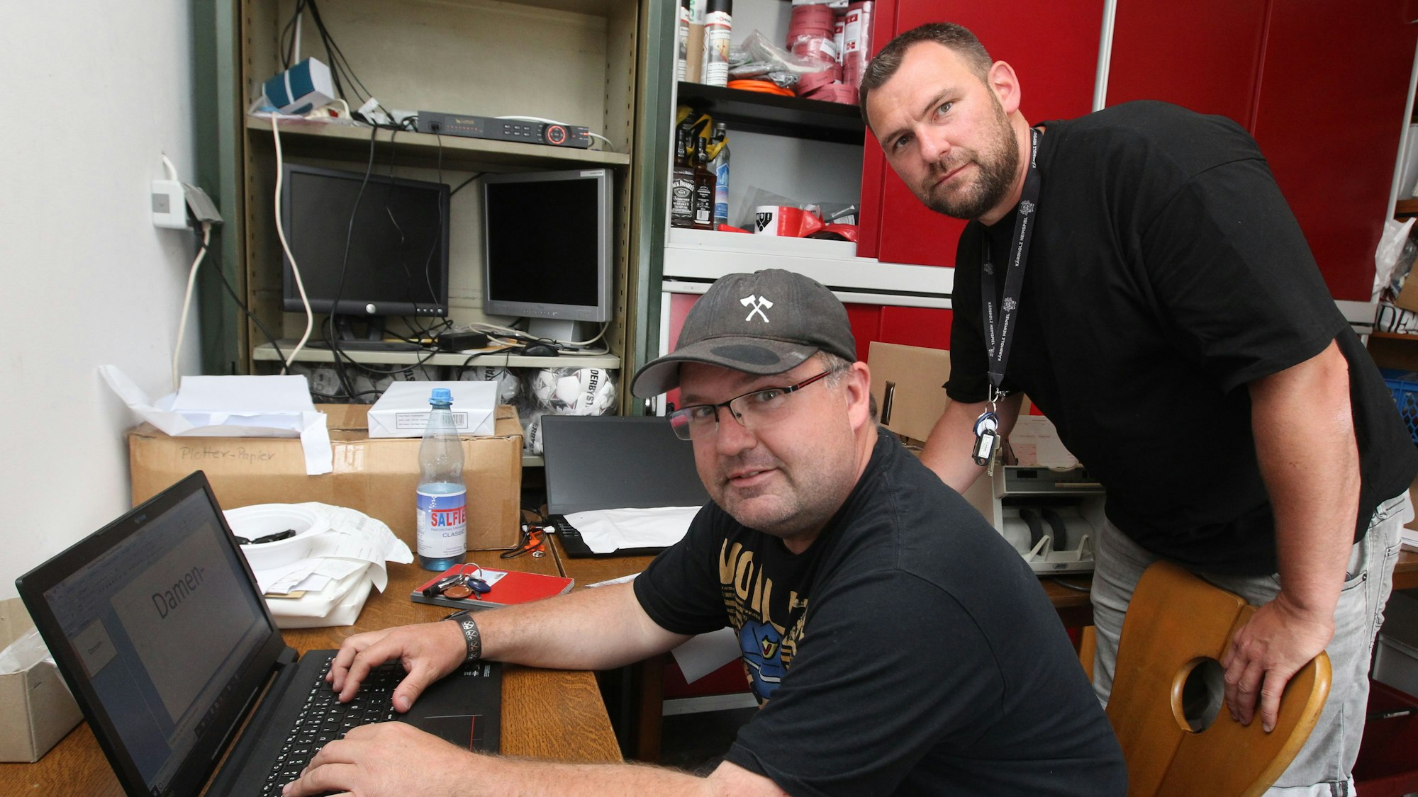 Zwei Männer sitzen an einem Laptop.