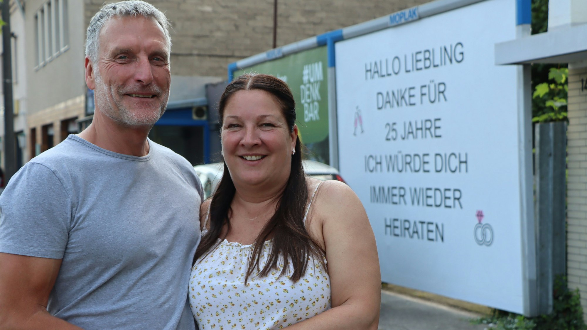 Auf dem Foto sind Michael und Heike Müller vor der Plakatwand mit der Liebesbotschaft zu sehen.