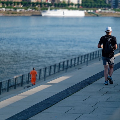 Zwei Jogger laufen in der frischen Morgenluft auf der Rheinpromenade am Rhein entlang.