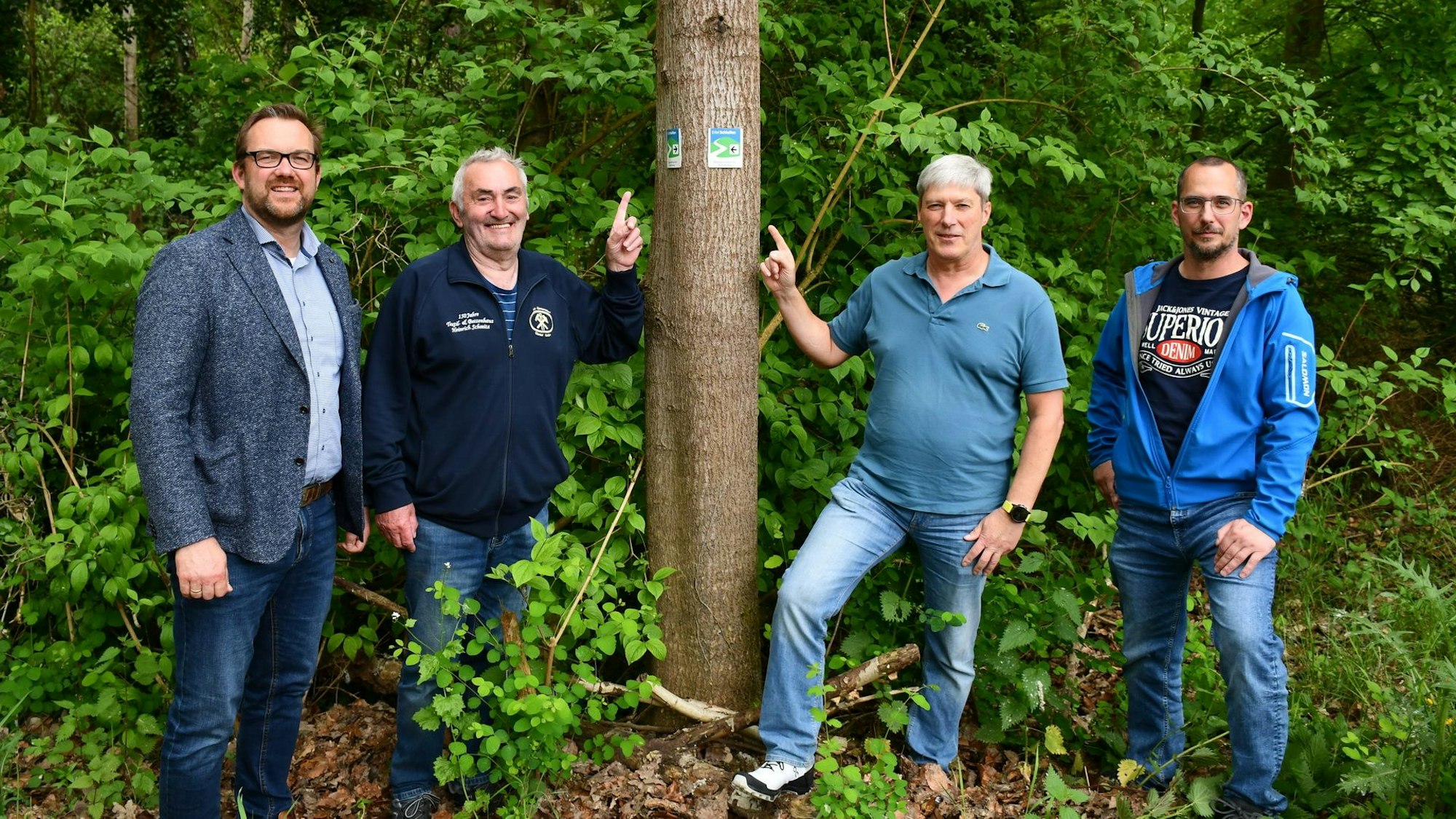 Beigeordneter Thomas Hambach (v.l.), Bergbaumuseumschef Günter Nießen, Eifelvereins-Wegewacht Michael Surbach und Constantin Hochgürtel vom Ordnungsamt an einem Baum mit einem Wanderwegweiser.