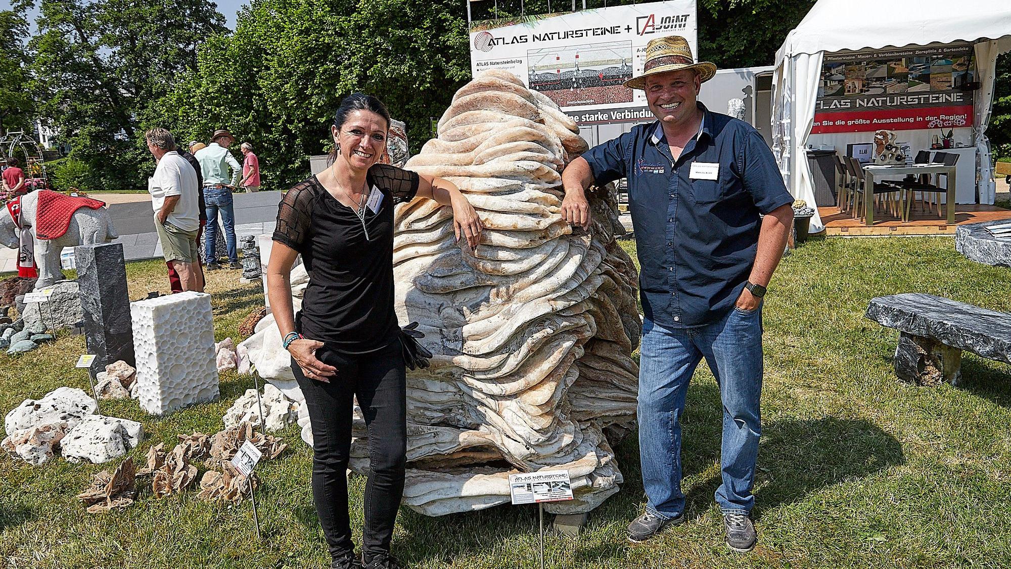 Das Bild zeigt eine Frau und einen Mann, die an einer großen Naturstein-Skulptur lehnen.