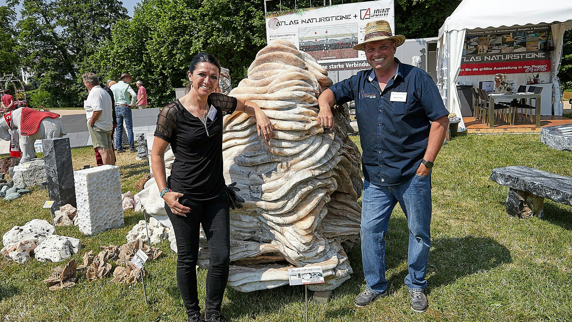 Das Bild zeigt eine Frau und einen Mann, die an einer großen Naturstein-Skulptur lehnen.