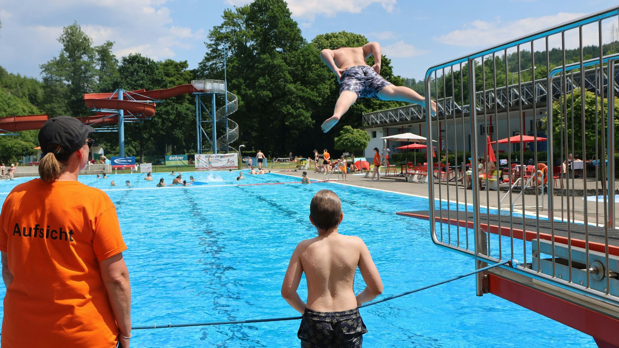 Jugendlicher springt im Freibad unter Aufsicht der Aufsicht ins Becken.