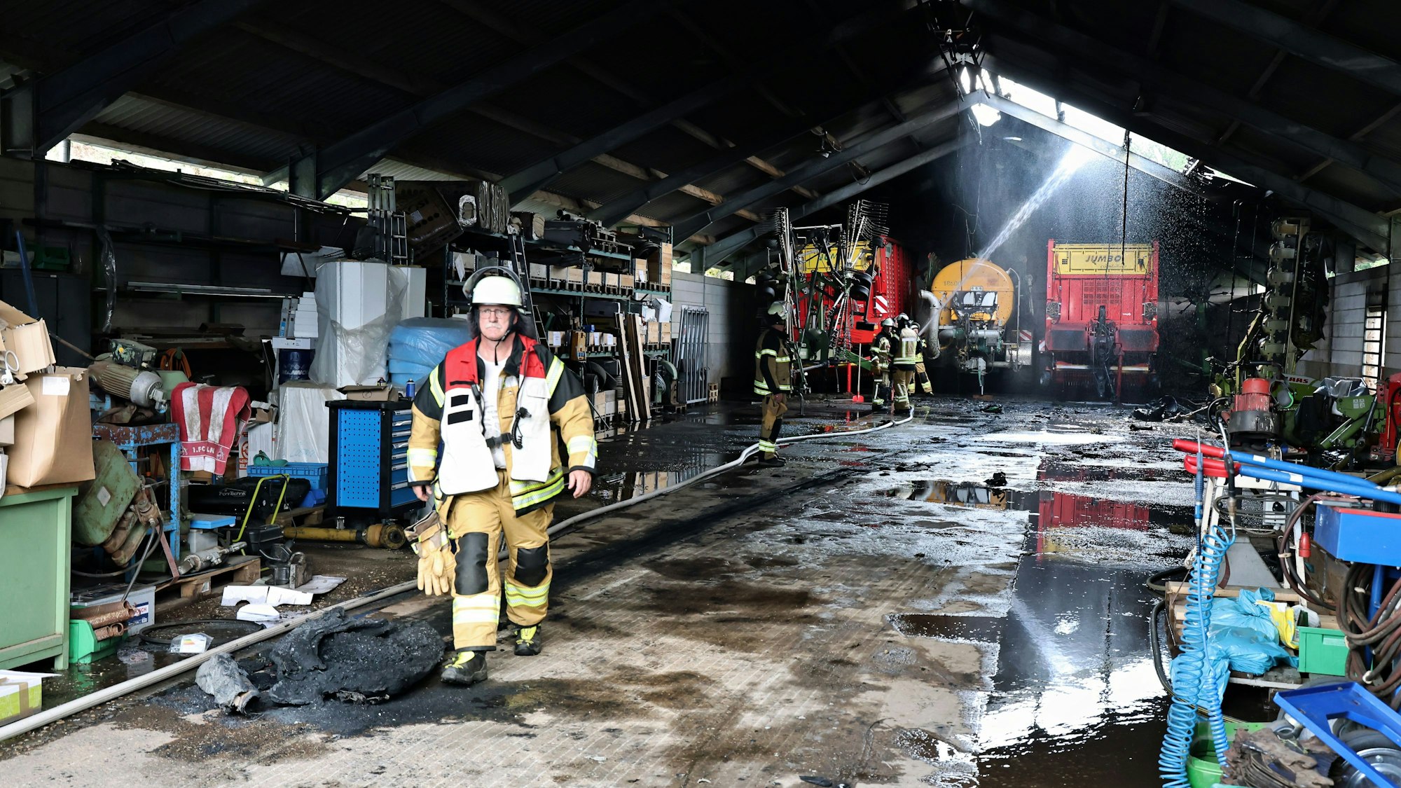 Feuerwehrleute löschen letzte Brandnester im Inneren der großen Scheune, in der es gebrannt hat.