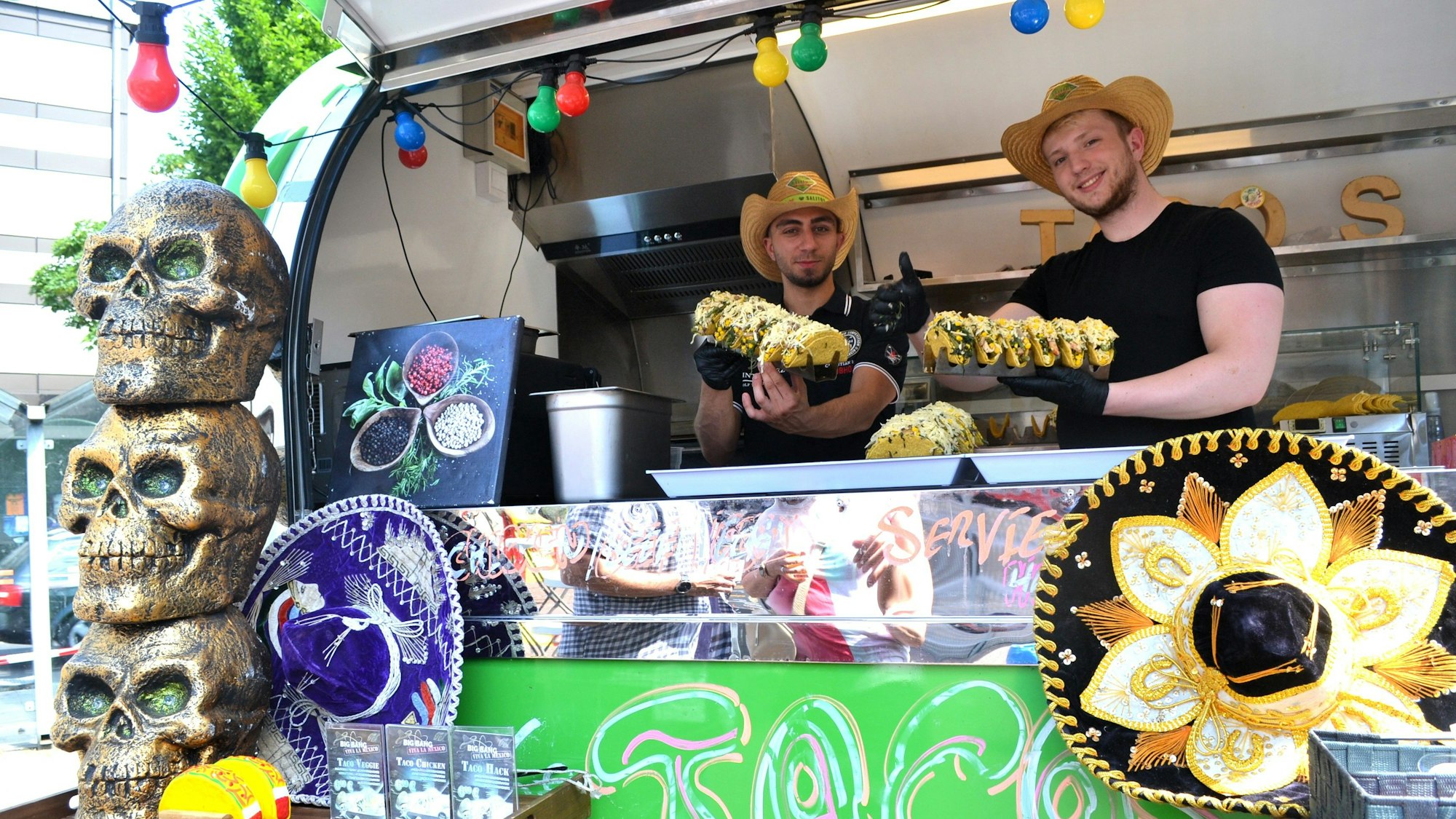 Zwei Männer mit Strohhüten stehen in einem Streetfood-Truck.