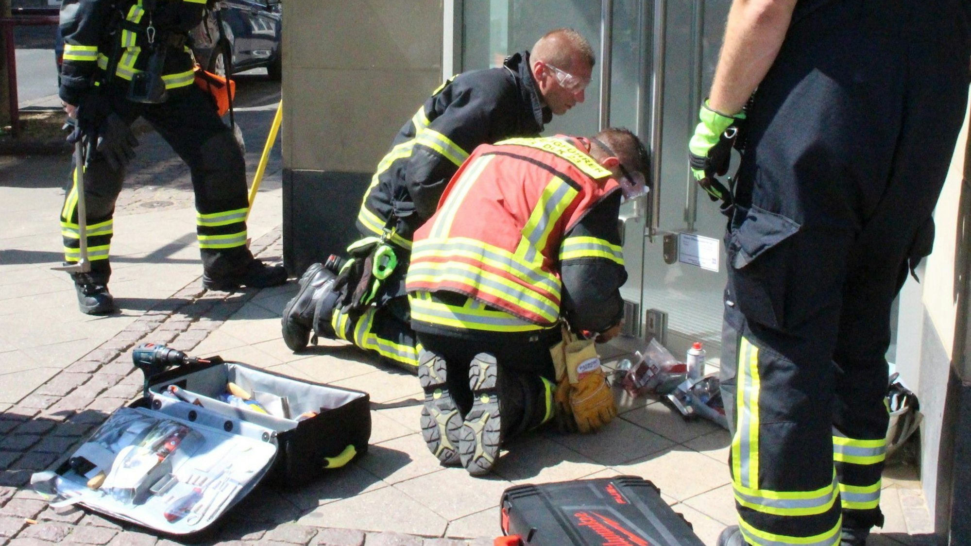 Zwei Feuerwehrleute knien vor der Eingangstür zu einem Geschäft in Euskirchen, die sie öffnen müssen, weil eine Einbruch-Nebel-Anlage ausgelöst hatte.