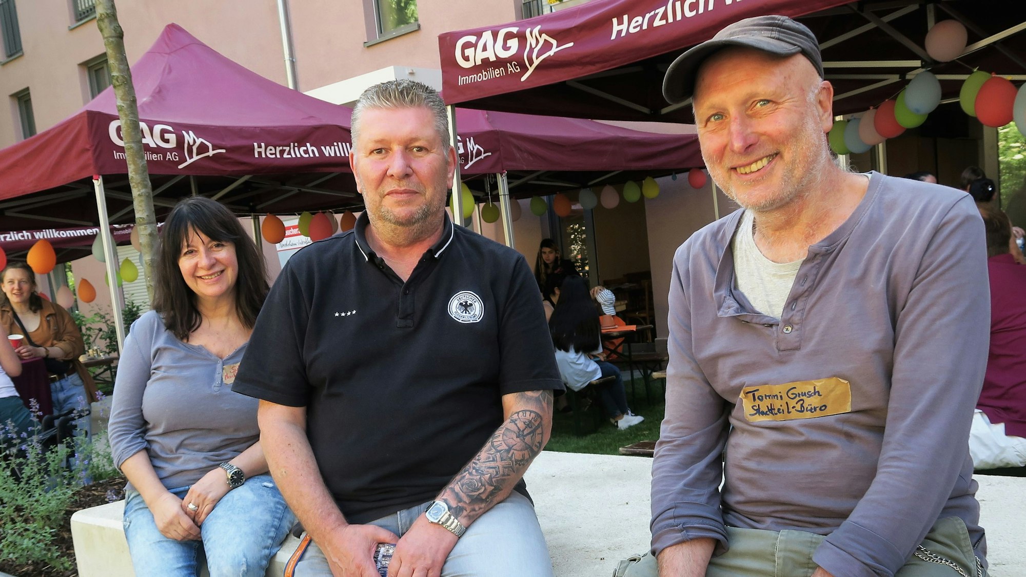 Eine Frau und zwei Männer sitzen vor einem Stand der GAG.