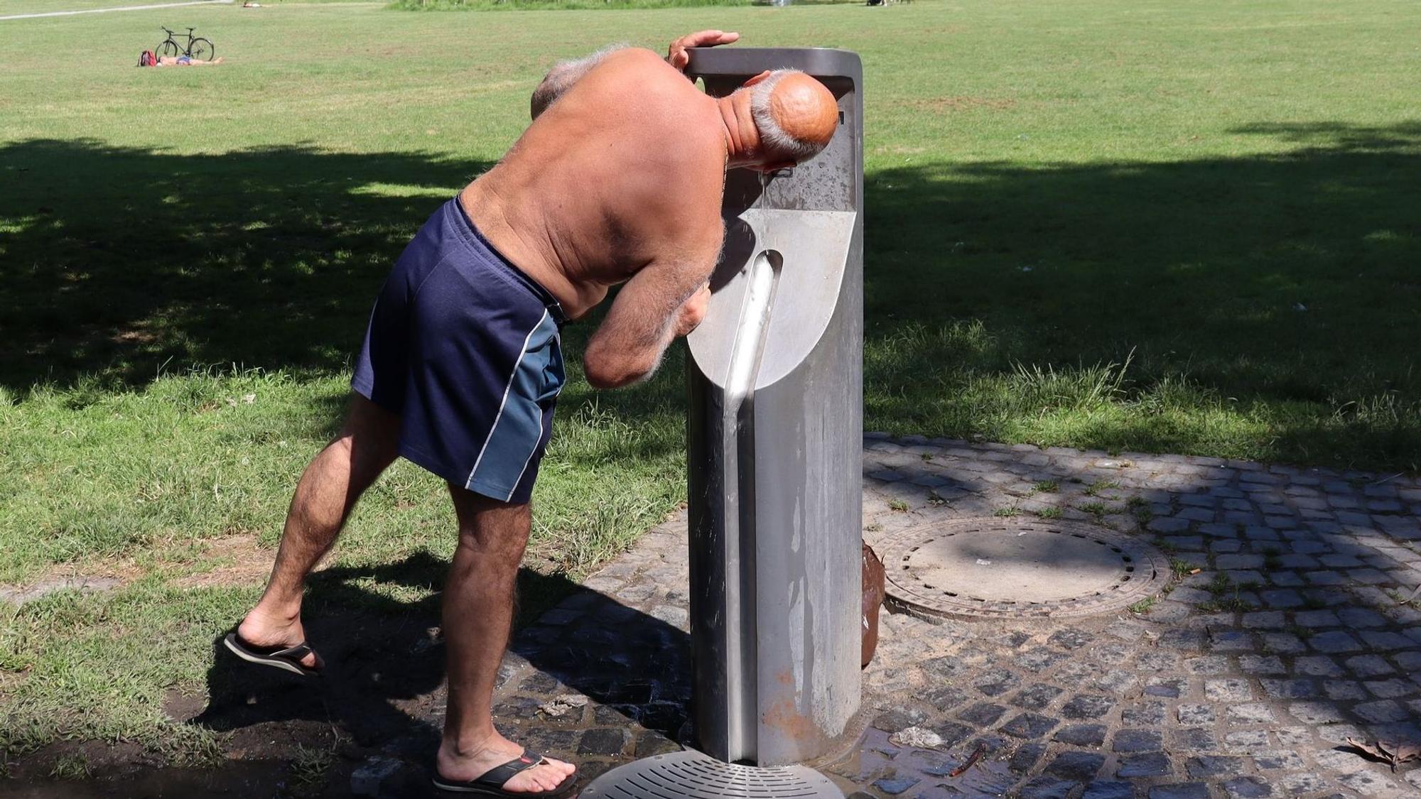 Ein Mann trinkt im Park aus einem Trinkwasserspender.