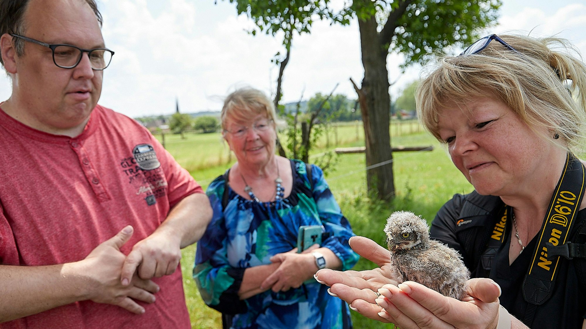 Drei erwachsene Besucher streicheln und betrachten ein Steinkauz-Küken.