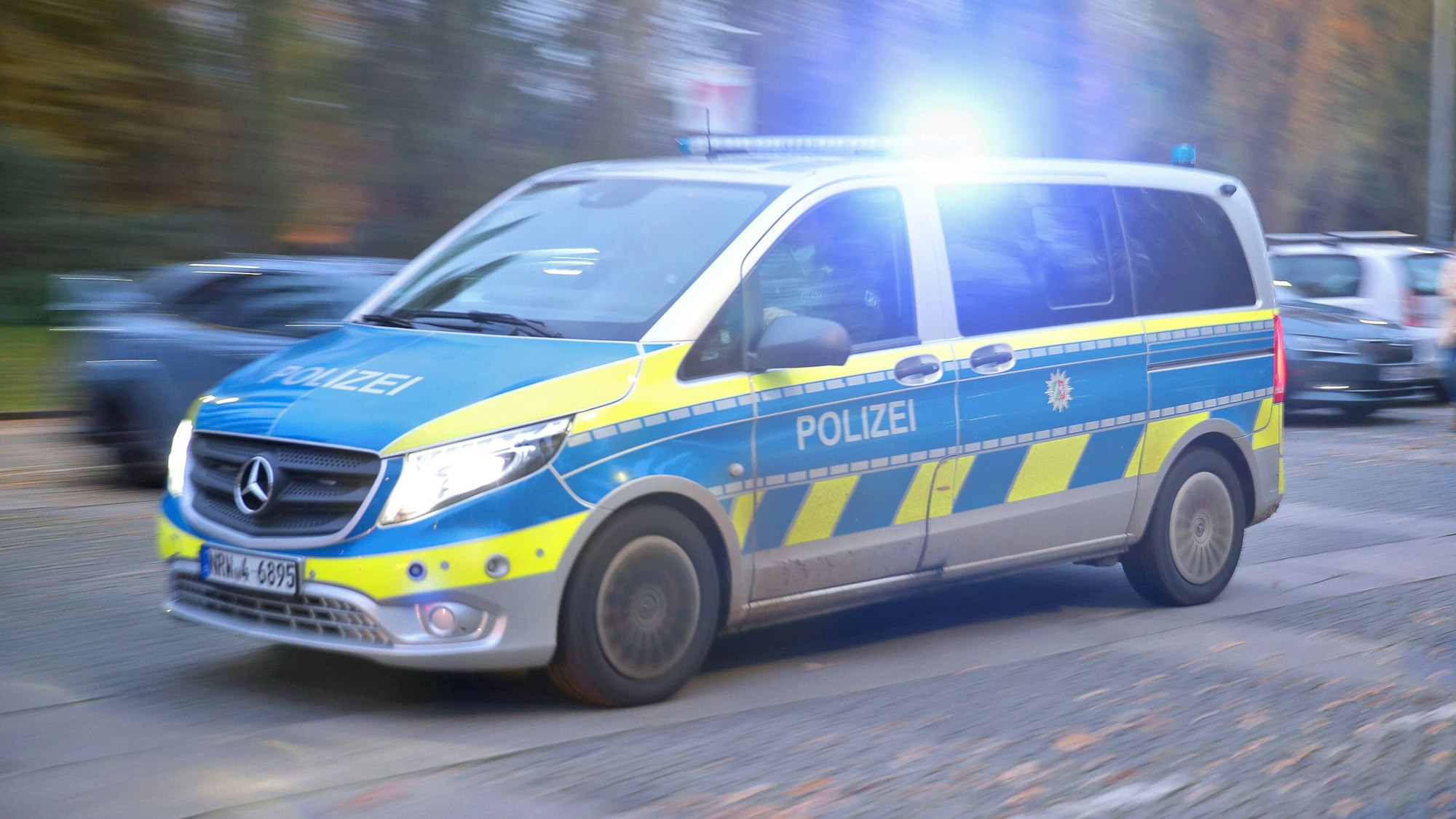 Ein Polizeifahrzeug der Landespolizei von NRW fährt mit Blaulicht auf einer Straße.