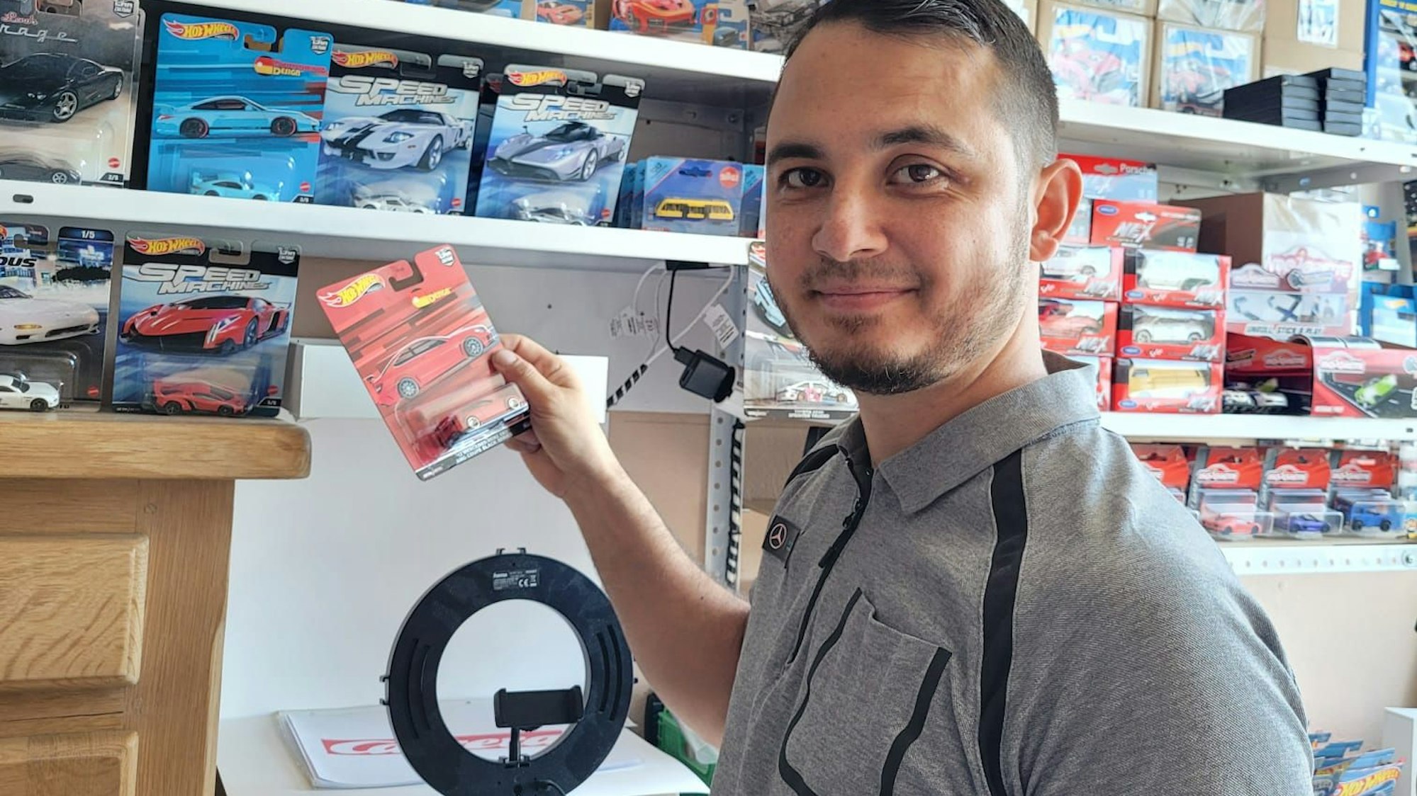Ozan Demir steht vor einem Regal mit zahlreichen Fahrzeugen. Er hält einen roten Sportwagen in der Hand.