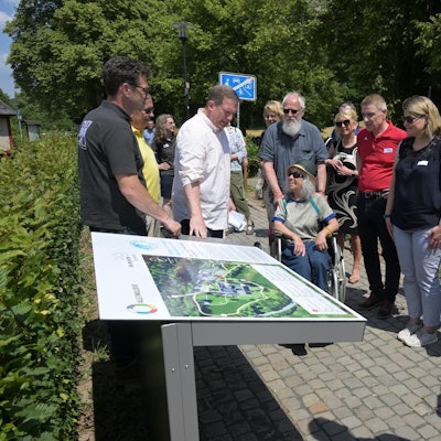 Menschen im Rollstuhl und ohne blicken auf eine Infotafel.
